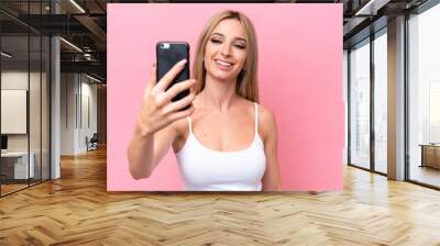 Pretty blonde woman isolated on pink background making a selfie with mobile phone Wall mural