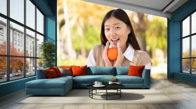 Pretty Chinese woman at outdoors holding an orange with surprised expression Wall mural