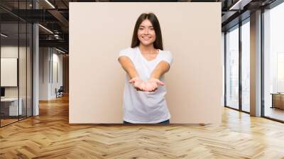 Pretty young girl over isolated background holding copyspace imaginary on the palm to insert an ad Wall mural