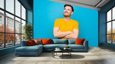 Redhead man over blue wall looking up while smiling Wall mural