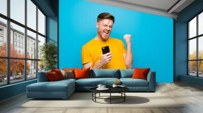 Redhead man over blue wall with phone in victory position Wall mural