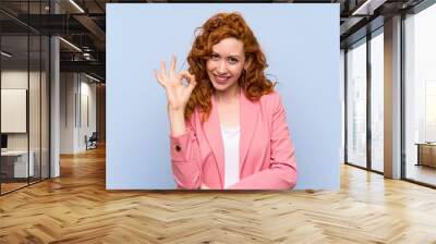 Redhead woman in suit over isolated blue wall showing ok sign with fingers Wall mural