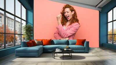 Redhead woman in suit over isolated pink wall making strong gesture Wall mural