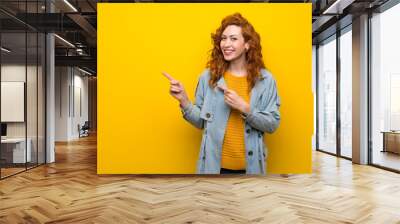 Redhead woman over isolated yellow background pointing finger to the side Wall mural