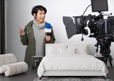 Reporter Vietnamese woman holding a microphone and reporting news pointing finger to the laterals and happy Wall mural