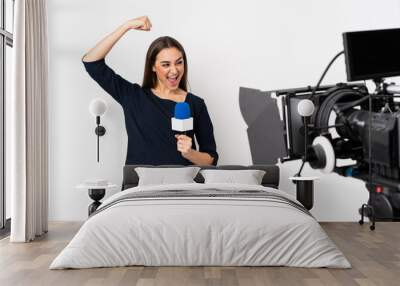 Reporter woman holding a microphone and reporting news isolated on white background celebrating a victory Wall mural