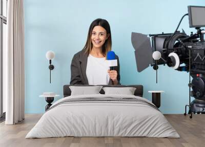 Reporter woman holding a microphone and reporting news over isolated blue background extending hands to the side for inviting to come Wall mural