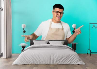 Restaurant waiter man over isolated blue background pointing finger to the laterals and happy Wall mural