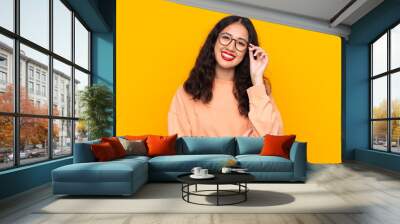 Spanish Chinese woman over isolated yellow background with glasses and happy Wall mural