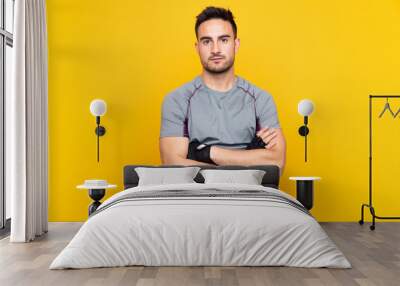 Sport man over isolated yellow wall with arms crossed Wall mural