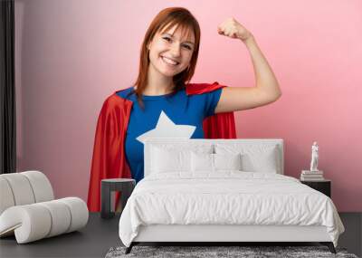 Super Hero redhead girl isolated on pink background doing strong gesture Wall mural