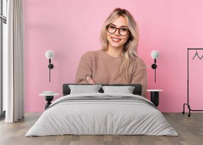 Teenager blonde girl wearing a sweater over isolated pink background with glasses and smiling Wall mural