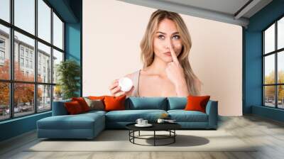 Teenager blonde girl with moisturizer over isolated background Wall mural