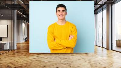 Teenager caucasian handsome man isolated on purple background keeping the arms crossed in frontal position Wall mural