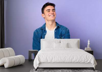 Teenager caucasian  handsome man isolated on purple background looking up while smiling Wall mural