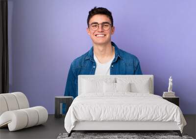 Teenager caucasian  handsome man isolated on purple background with glasses and happy Wall mural