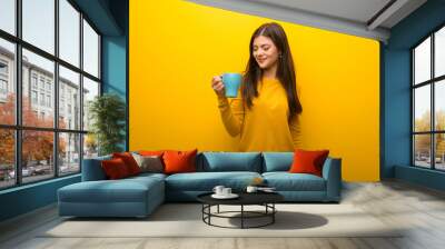 Teenager girl on vibrant yellow background holding a hot cup of coffee Wall mural