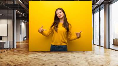 Teenager girl on vibrant yellow background proud and self-satisfied in love yourself concept Wall mural