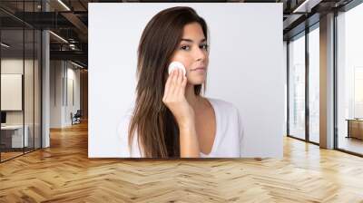 Teenager girl over isolated background with cotton pad for removing makeup from her face Wall mural