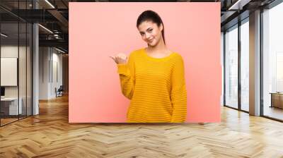 Teenager girl  over isolated pink wall pointing to the side to present a product Wall mural