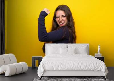 Teenager girl over isolated yellow wall doing strong gesture Wall mural