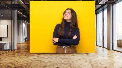 Teenager girl over isolated yellow wall looking up while smiling Wall mural