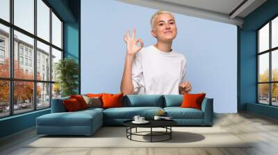 Teenager girl with white short hair over blue wall showing ok sign with fingers Wall mural