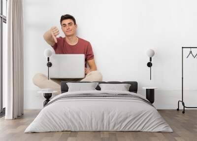 Teenager man sitting on the flor with his laptop showing thumb down with negative expression Wall mural