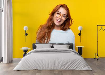 Teenager redhead girl over isolated yellow background with glasses and happy Wall mural