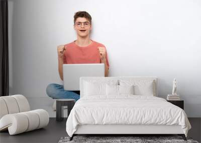 Teenager Russian man holding pc sitting on the floor isolated on white background celebrating a victory in winner position Wall mural