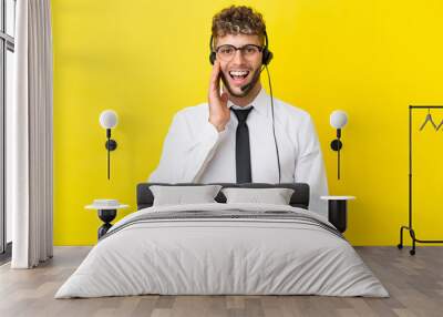 Telemarketer blonde man working with a headset isolated on yellow background with surprise and shocked facial expression Wall mural