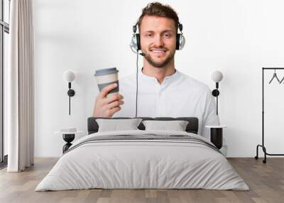 Telemarketer caucasian man working with a headset over isolated chroma key background holding coffee to take away and a mobile Wall mural