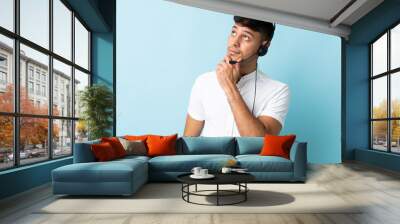 Telemarketer Colombian man working with a headset over isolated background and looking up Wall mural