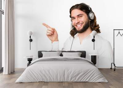 Telemarketer man working with a headset over isolated chroma key background pointing finger to the side and presenting a product Wall mural