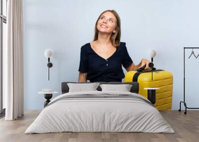 Traveler blonde woman with suitcase looking up while smiling Wall mural