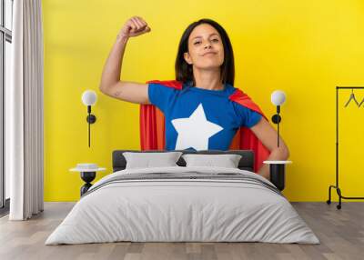 Woman isolated on yellow background in superhero costume and doing strong gesture Wall mural