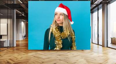 Woman with christmas hat isolated on blue background looking to the side Wall mural