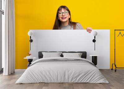 Woman with glasses over yellow wall holding an empty white placard Wall mural