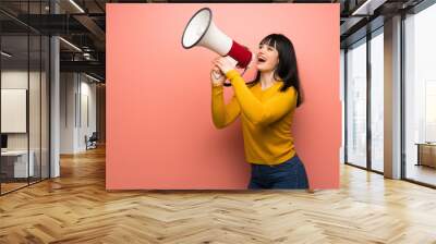 Woman with yellow sweater over pink wall shouting through a megaphone Wall mural