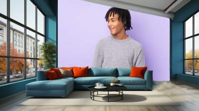 Young african american man isolated on purple background looking side Wall mural