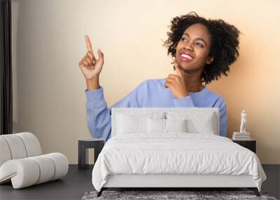 Young African American woman isolated on beige background pointing with the index finger a great idea Wall mural