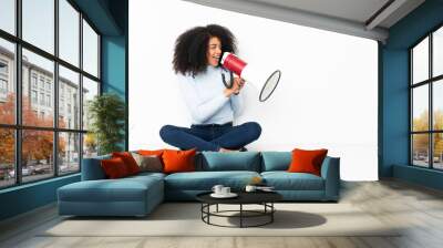 Young african american woman sitting on the floor shouting through a megaphone Wall mural