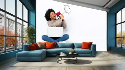 Young African American woman with a laptop sitting on the floor shouting through a megaphone Wall mural