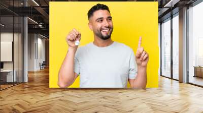 Young Arab man holding home keys isolated on yellow background intending to realizes the solution while lifting a finger up Wall mural