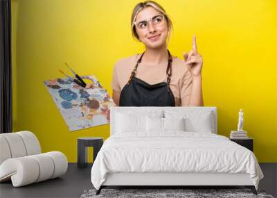 Young artist caucasian woman holding a palette isolated  on yellow background pointing up a great idea Wall mural