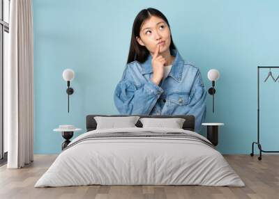 Young asian woman isolated on background having doubts while looking up Wall mural