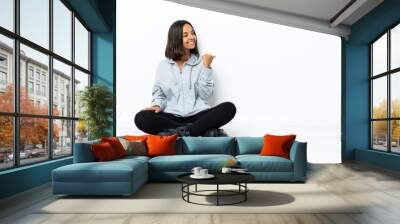 Young asian woman with roller skates on the floor pointing to the side to present a product Wall mural