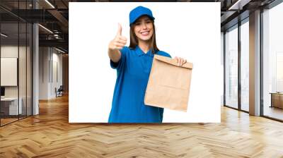 Young beautiful caucasian woman taking a bag of takeaway food over isolated background with thumbs up because something good has happened Wall mural