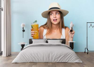 Young beautiful woman holding a cocktail isolated on blue background intending to realizes the solution while lifting a finger up Wall mural