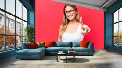 Young beautiful woman isolated on red background showing and lifting a finger Wall mural